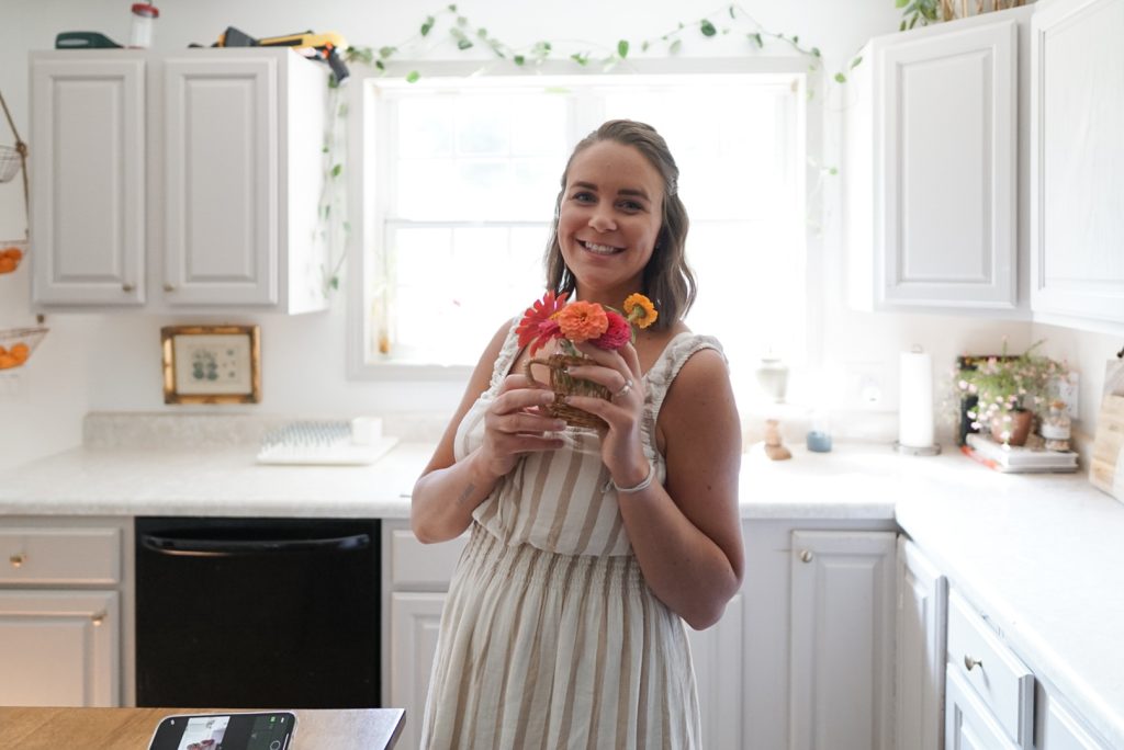 Woman standing in sunlit kitchen with cut flowers in her hand