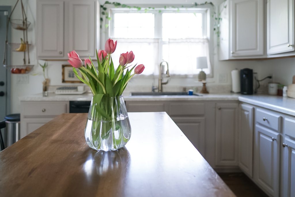 vase of tulips on kitchen island with a bright window in background