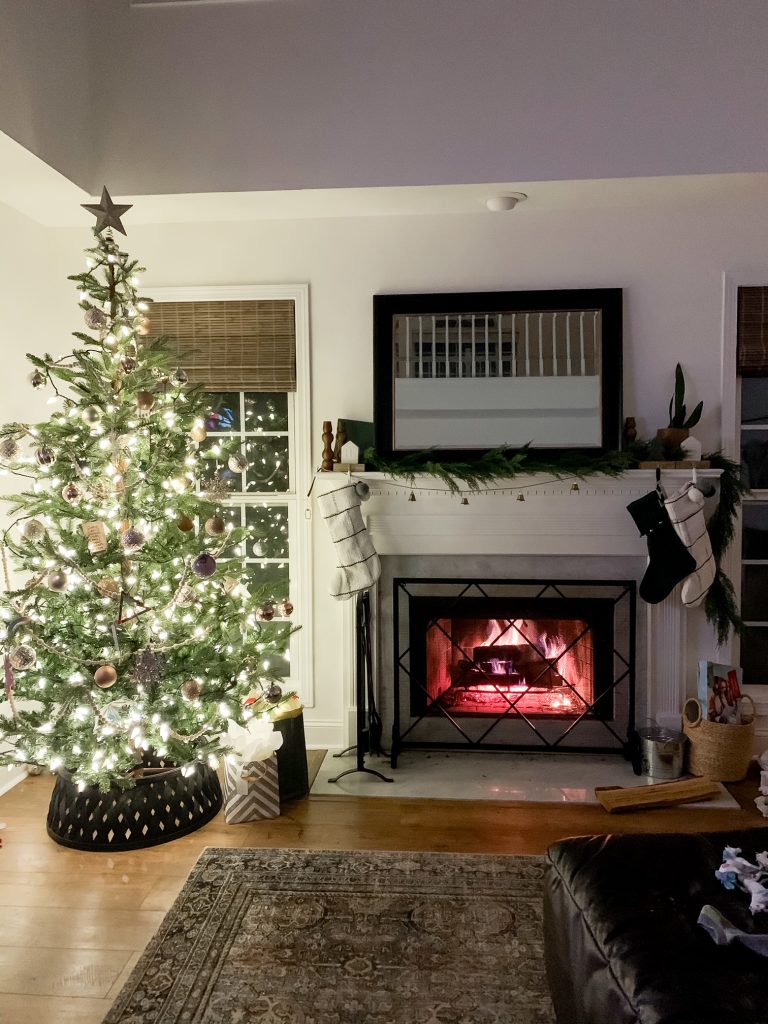 Christmas tree lit up at night next to wood burning fireplace
