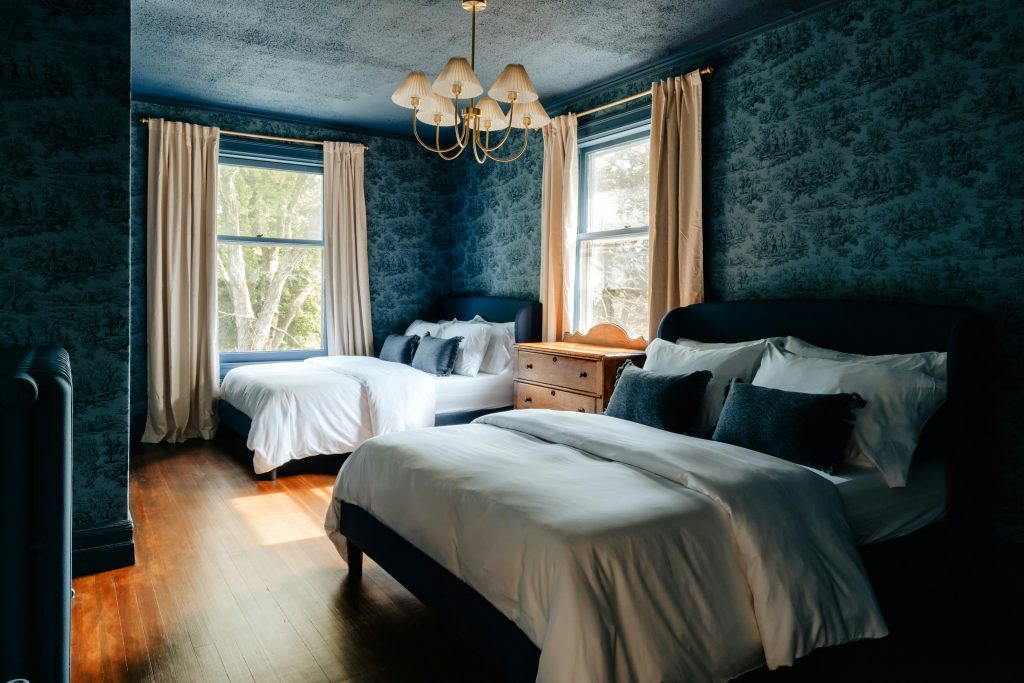 large bedroom with dark blue vintage style floral wallpaper and two double beds 