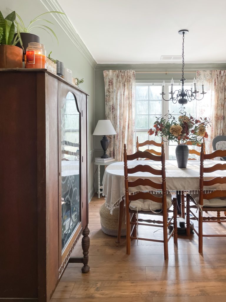 Dining room with floral curtains over a double window. Vintage dining set and classic chandelier with vase of florals on table.