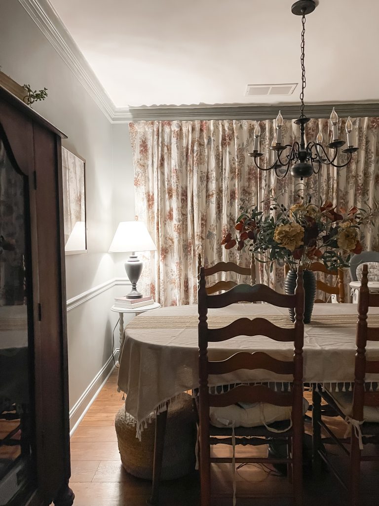 Cottage style dining room with antique furnishings and floral curtains along the back wall