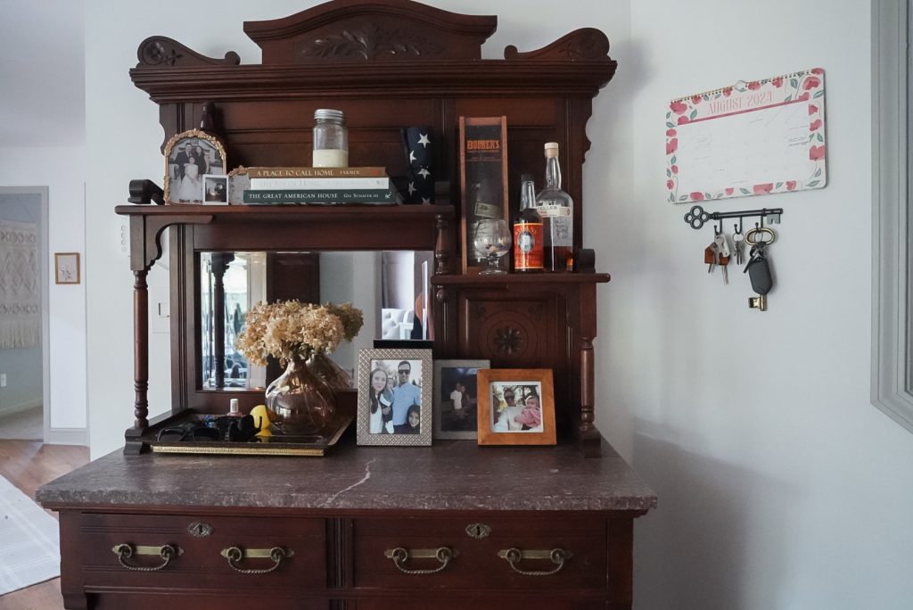 Antique dark wood bar cabinet used as an entry table with framed photos and a family calendar in view