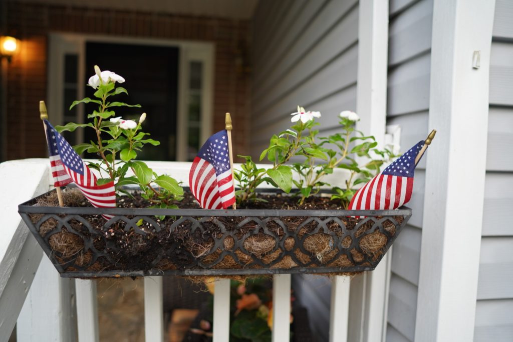 Porch railing flower box with white flowers and small American Flag decor