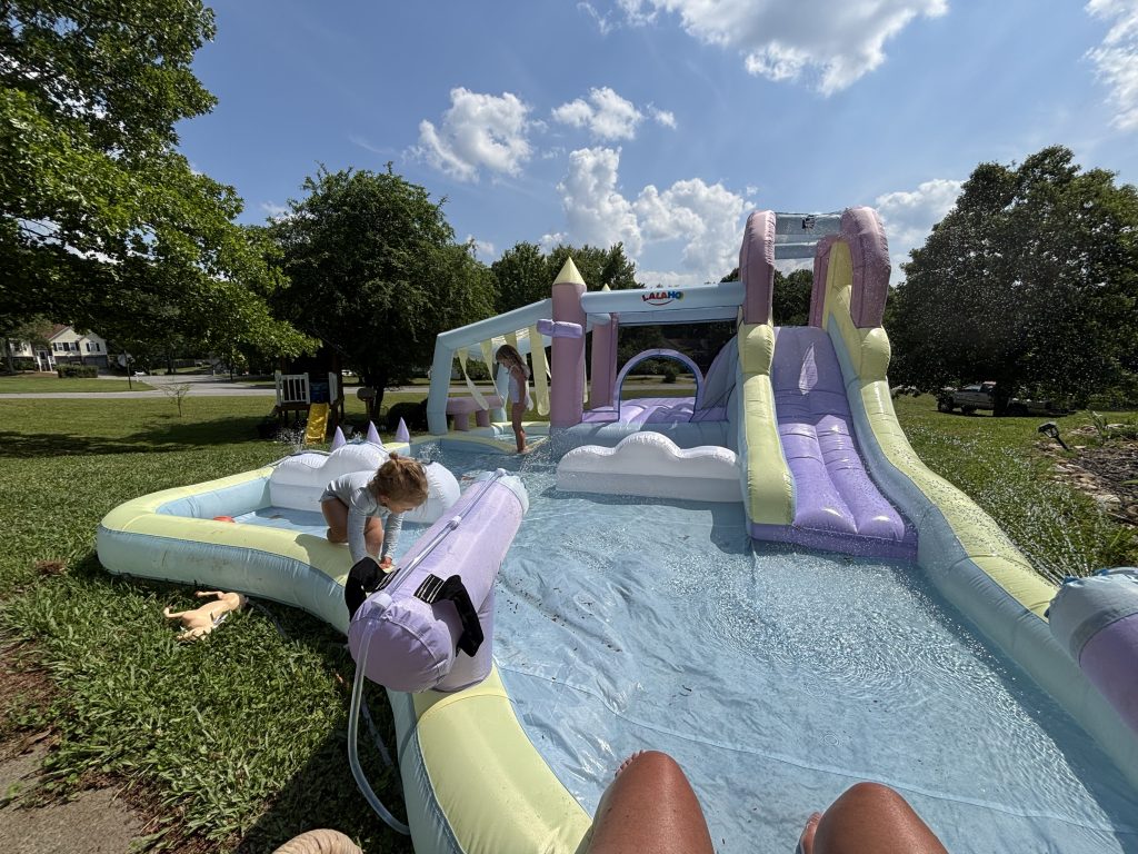young kids playing outside in summer on inflatable pool slide