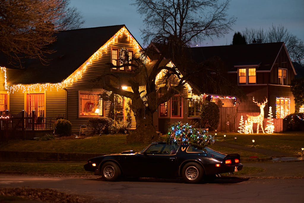 A classic car parked near houses decorated with Christmas lights and a festive atmosphere.