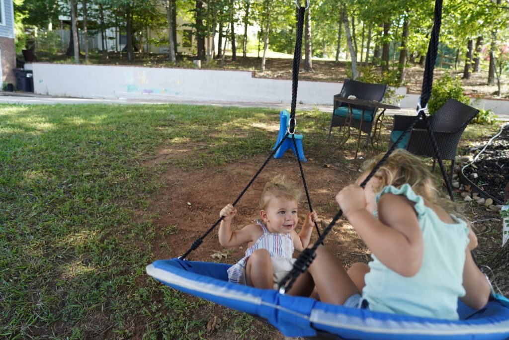 Young kids outside playing on a round swing hanging from a large tree 