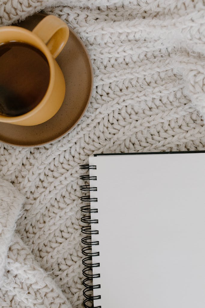 Warm coffee cup on a knitted blanket beside an open notebook, ready for inspiration.